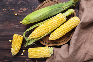 Board with fresh corn cobs on dark wooden table