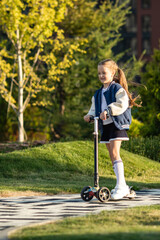 Child little girl riding scooter on the sidewalk in a city park. Active outdoor fun for kids....