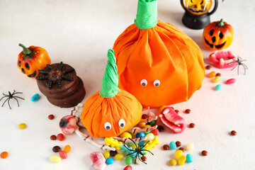 Paper pumpkins for Halloween and tasty candies on light background