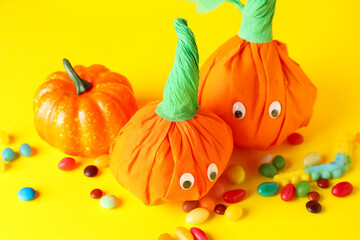 Paper pumpkins for Halloween and tasty candies on color background, closeup
