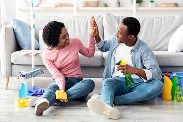 Satisfied young african american man and woman house-keepers sitting on floor in living room and...