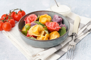Bowl of boiled colorful dumplings with spinach and tomatoes on white background