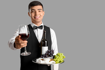Young sommelier with wine and snacks on grey background