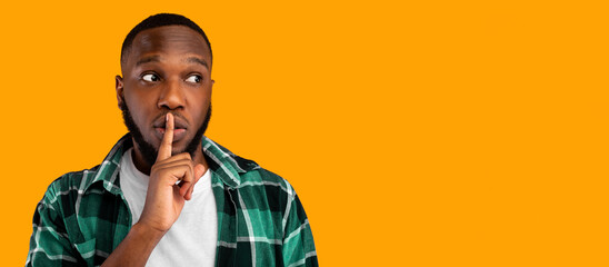 Shh, it's a secret. African american guy gesturing finger on lips looking aside at free space for...