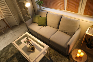 Interior of modern living room with grey sofa, burning candles and glowing lamp at evening