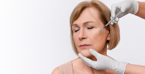 Elderly woman getting beauty injection on white studio background, panorama with copy space