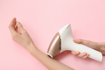 Female hands with photoepilator on pink background