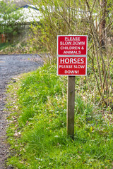 Slow down warning sign for children, animals, and horses on rural road