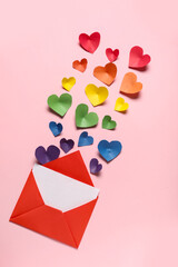 Paper hearts in colors of LGBT flag and envelope on pink background. Valentine's Day celebration