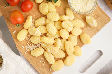 Wooden board with tasty gnocchi, tomatoes and grated cheese on light background