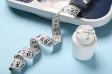 Bottle with weight loss pills, scales and measuring tape on blue background