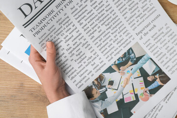 Female hand holding newspaper on wooden background
