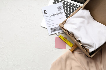Open parcel with clothes, label and laptop on white table
