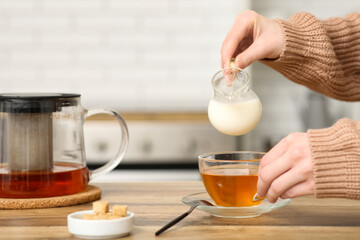 Young woman pouring milk in cup of tea in kitchen