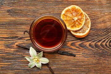 Bowl of vanilla extract, sticks and dried orange slices on wooden background