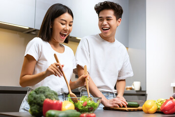 Joyful Chinese Couple Cooking Food And Laughing Preparing Salad For Dinner Together In Kitchen At Home On Weekend. Asian Husband And Wife Cook Meal. Healthy Nutrition And Family Recipes Concept
