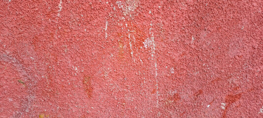 Close-up of an old painted red concrete wall with rough texture, peeling paint, uneven and grungy...