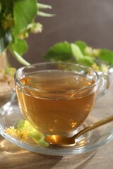 Tasty linden tea in cup, spoon, leaves and flowers on wooden table against grey background, closeup