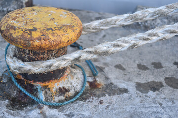 white rope on an iron pole. A thick white rope is wrapped around a green metal bollard, securing a...