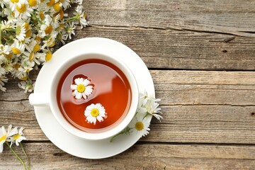 Aromatic tea in cup and chamomile flowers on wooden table, flat lay. Space for text