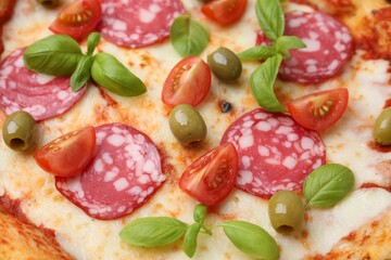 Delicious pizza with salami, olives, tomatoes and basil as background, closeup