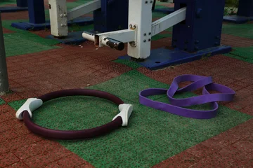 Gordijnen Gym equipment objects in outdoor urban street sport ground with safe rubber surface green red colors. Pilates ring, fitness band lying on the floor with no people. Closeup © Anastasia.photoyoga