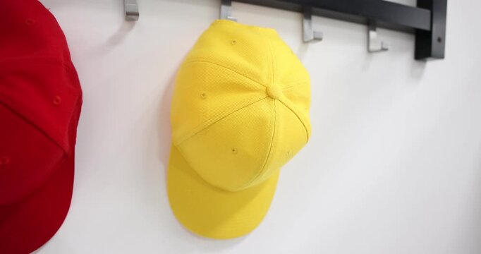 Woman taking light blue baseball cap from hook rack on white wall, closeup
