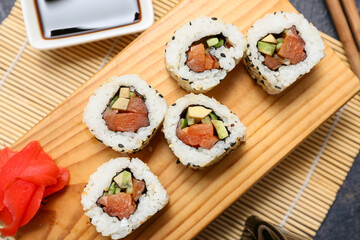 Board with tasty sushi rolls, soy sauce and marinated ginger on bamboo mat, closeup