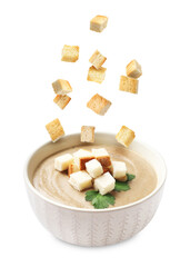 Croutons falling into bowl of soup against white background