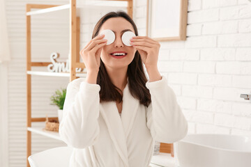 Happy young woman removing makeup with cotton pads in bathroom