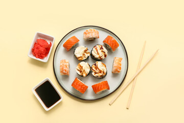 Tasty sushi rolls with chopsticks, marinated ginger and soy sauce on light yellow background