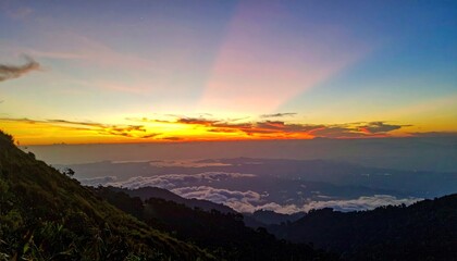 Obraz premium Majestic mountain vista at dawn with radiant sunlight breaking through clouds