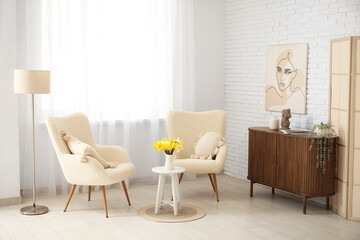 Comfortable armchairs and coffee table with daffodil flowers in interior of living room