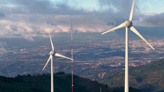 Beautiful aerial footage of wind Mills - turbines- on Costa Rica’s hills at sunset, overlooking San José city with vibrant skies, renewable energy, and a stunning mountain landscape - Powered by Adobe