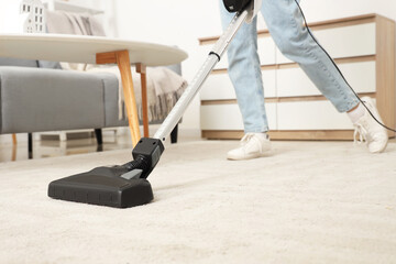 Young woman cleaning carpet with cordless stick vacuum cleaner in living room, closeup