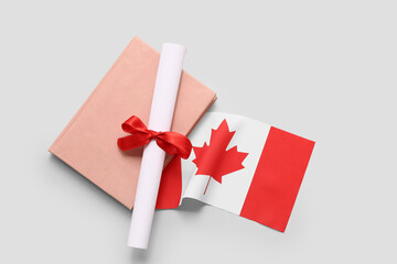 Diploma with red ribbon, Canadian flag and book on grey grunge background