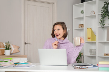 Thoughtful female student with cup studying at home