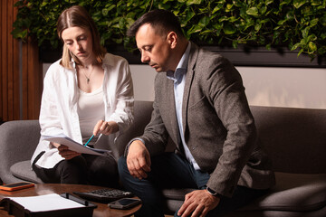 Two business colleagues discuss documents intently on a modern sofa. Professional teamwork,...