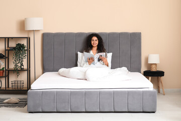 Young African-American woman reading magazine on soft mattress at home
