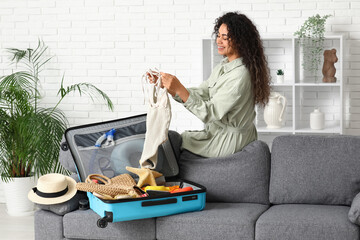 Beautiful young woman unpacking summer clothes from suitcase at home