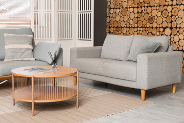 Interior of living room with grey sofa, coffee table, lamp and folding screen near wooden wall