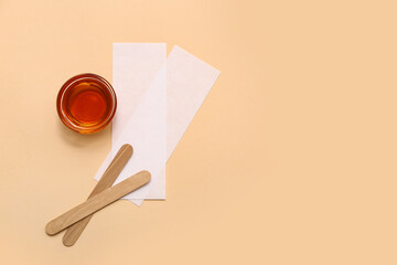 Glass bowl with sugaring paste, wax strips and wooden sticks on beige background