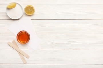 Glass bowl with sugaring paste, wax strips and sticks on white wooden background