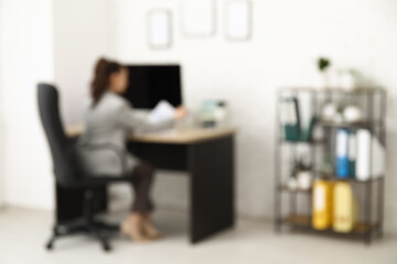 Female office worker sitting on armchair at workplace in light office, blurred view