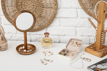 Stands with different stylish jewelry, perfume bottle and mirror on dresser near white brick wall