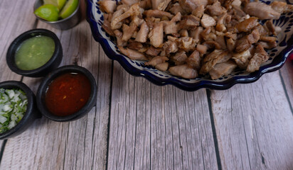 Top view of a table with a plate of pork carnitas and some salsas on the side (Mexican food)