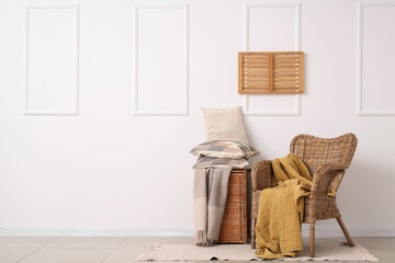 Wicker armchair and basket with stack of pillows near white wall