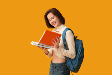 Beautiful female student with notebooks and backpack on yellow background