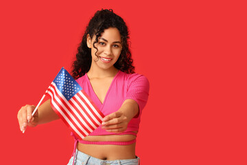Beautiful young happy African-American woman with USA flag on red background