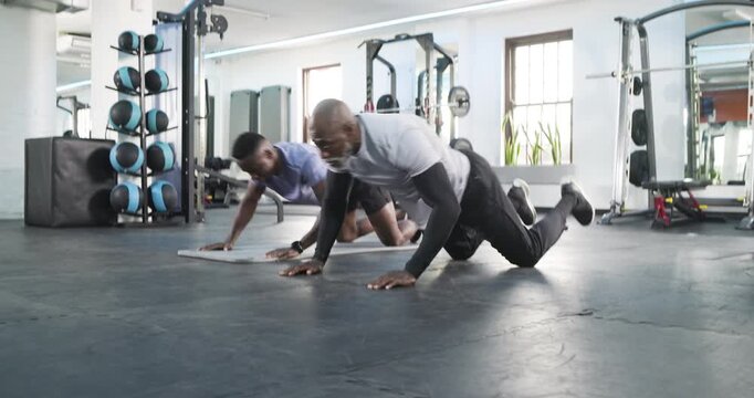 Entering gym African American coach guiding man through push-up, hip bridge on mat for strength
